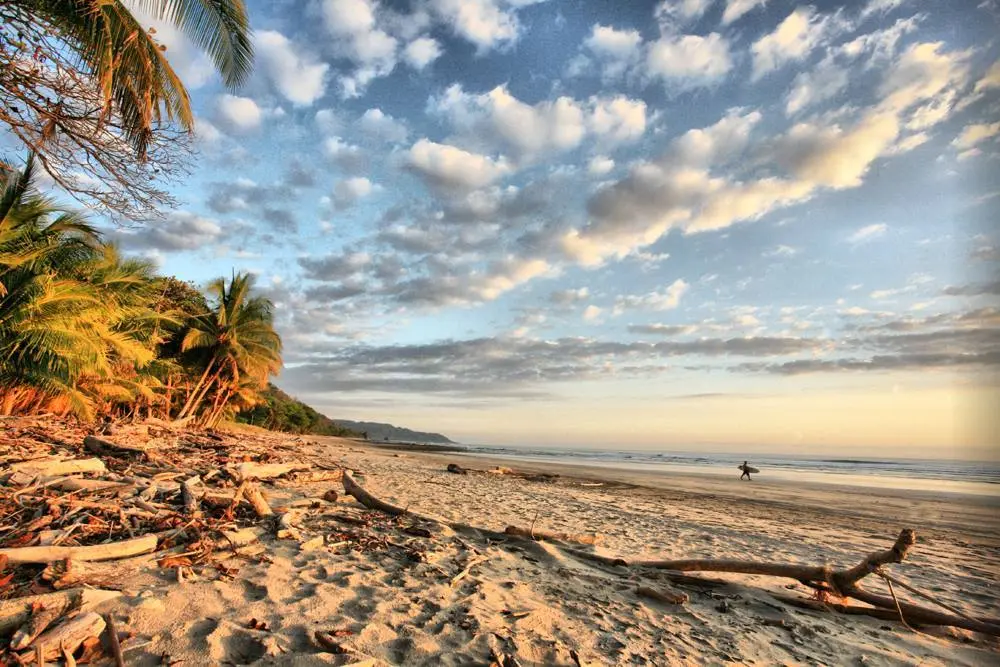 Atardecer con surfista caminando por la arena de Playa Hermosa